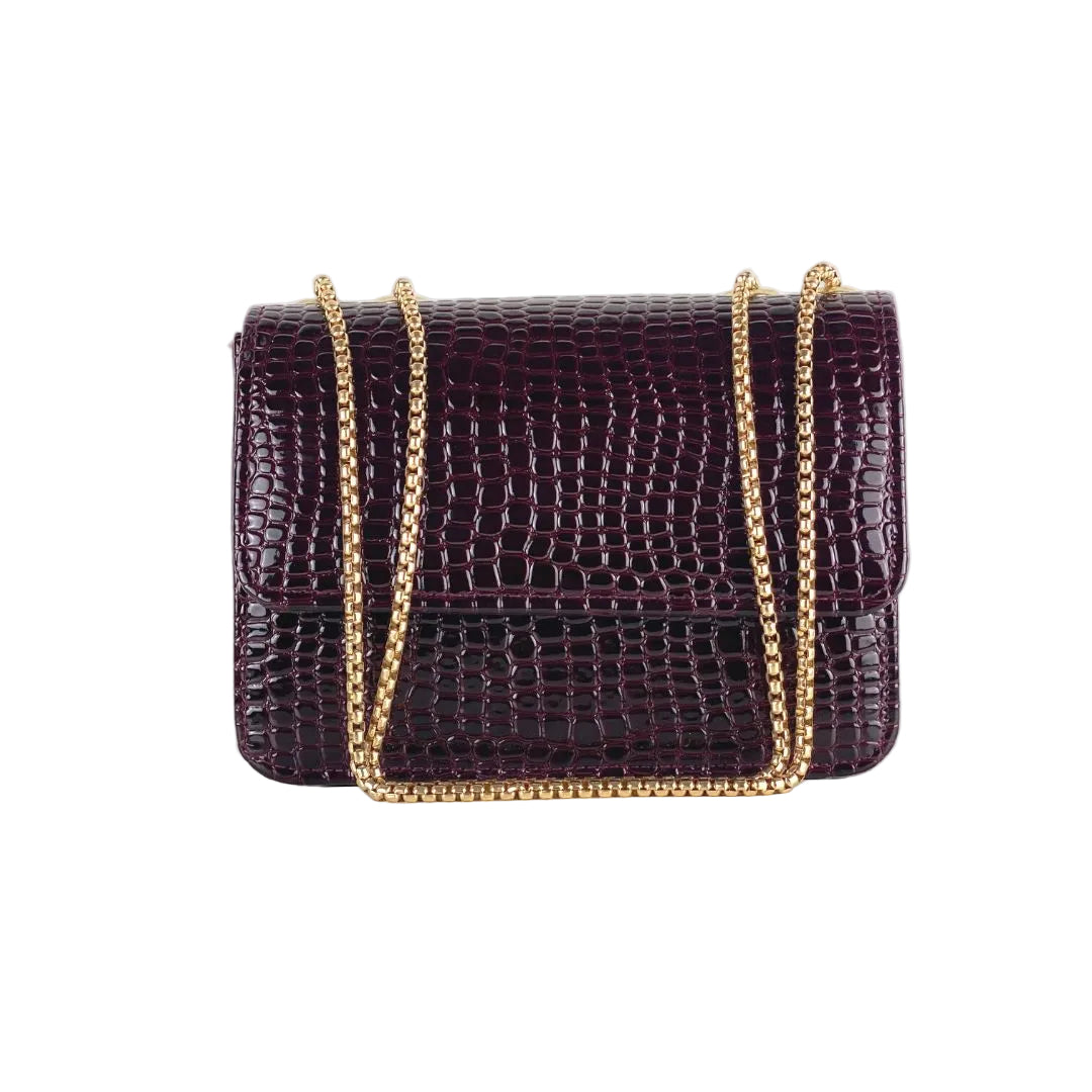 Purple crocodile-patterned handbag with gold chain strap on a white background